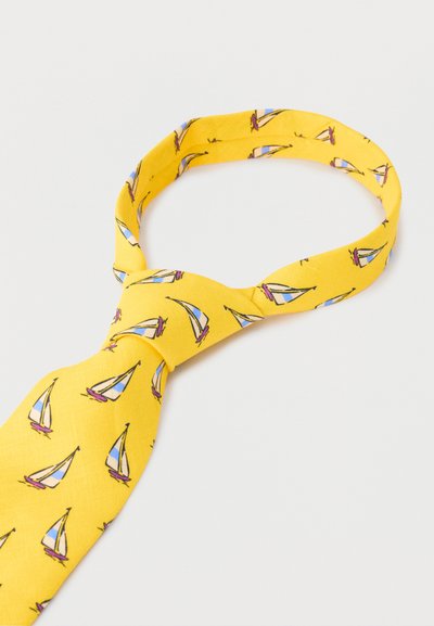 Κίτρινη γραβάτα με μοτίβα μπλε και λευκών ιστιοφόρων δεμένη σε κόμπο Ουίντσορ σε απλό φωτεινό φόντο.