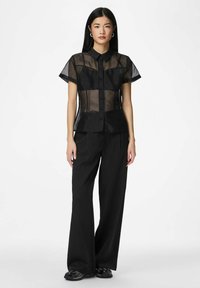 Blouse noire transparente à manches courtes avec boutons et coupe ajustée, associée à un pantalon large à fines rayures noir. Accentué par une texture subtile.