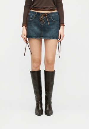 Inimene kannab sinist teksamini seelikut ees nööritava detailiga, pruuni pika varrukaga särk ja põlveni ulatuvaid tumedaid pruune nahksaapaid.