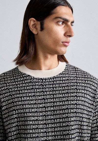 Pulover negru din tricot, cu un model repetat al logo-ului în alb, având un guler crem cu nervuri. Textură moale și design contemporan.