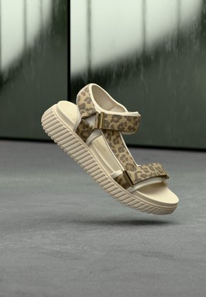 Sandales imprimé léopard avec des brides beiges, des accents de ferrures dorées et une semelle texturée et épaisse. Matière légère et design ouvert.