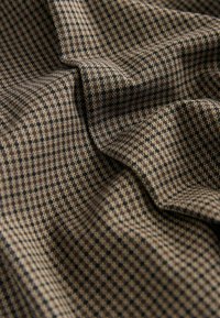 Tkanina w wzór houndstooth w odcieniach brązu, beżu i czerni, charakteryzująca się miękką teksturą i gładkimi fałdami.