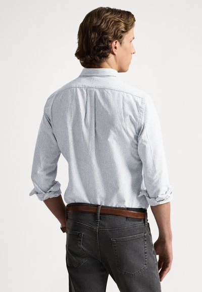 Πουκάμισο με ρίγες σε ανοιχτό μπλε και λευκό, με μανίκια γυρισμένα και πιέτες στην πλάτη, συνδυασμένο με σκούρα γκρι τζιν και καφέ ζώνη.