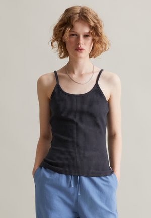 Black ribbed tank top with thin adjustable straps. Features a rounded neckline and fitted silhouette. Model wears light blue pants.