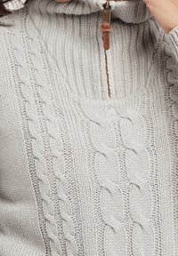 Maglione a maglia grigio chiaro con colletto alto, chiusura a mezzo zip e motivo a treccia sulla parte frontale. Texture morbida e design voluminoso.