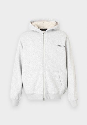 Grauer Reißverschluss-Hoodie aus weichem, strukturiertem Material, mit Fleece-Futter und zwei Vordertaschen. Kleines Logodetail auf der Brust.