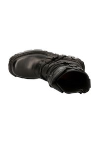 Botte en cuir noir avec un bout rond, des lacets et des boucles. Semelle robuste avec un profil de crampons prononcé. Design à cheville haute. Texture lisse.