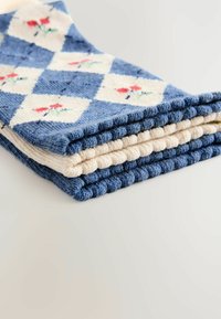 Gefalteter blauer und cremefarbener Stoff mit einem Diamantmuster und kleinen floralen Designs. Die Textur wirkt weich und einladend.