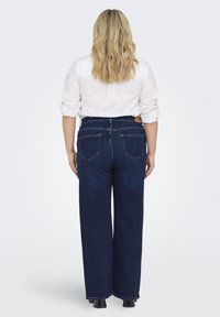 Dark blue wide-leg jeans with a high waist, featuring five pockets and a denim texture. Worn with a white button-up shirt.