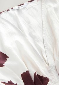 Weißes Kleid mit tiefem V-Ausschnitt und maroonfarbigen Pinselstrichmustern am Saum. Hergestellt aus leichtem Stoff mit weicher Textur.