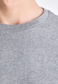 Camiseta de algodón gris con un cuello redondo acanalado. La tela presenta una textura suave y un sutil patrón jaspeado.