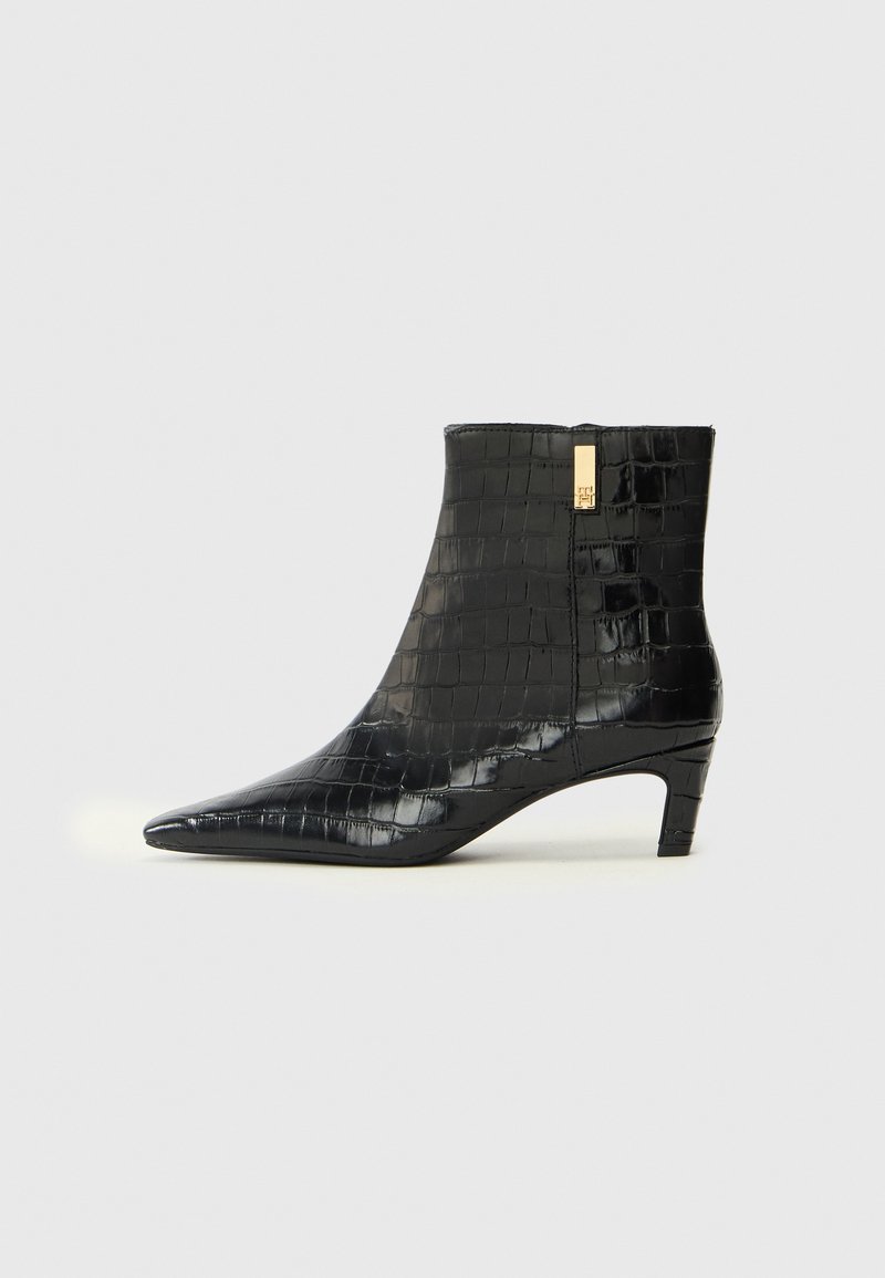 Bottines noires en matériau synthétique brillant avec une texture crocodile, bout pointu et petit talon. Accent doré à l'arrière.