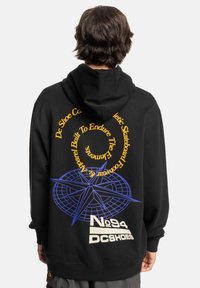 Zwarte hoodie van een katoenmix; heeft gele en blauwe grafische tekst en ontwerpen op de achterkant, inclusief een kompas en logo-accenten.