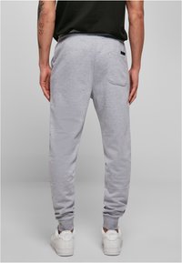 Pantalons de jogging gris en tissu doux, avec une coupe slim, des chevilles fuselées et une poche arrière. Associés à des baskets blanches.