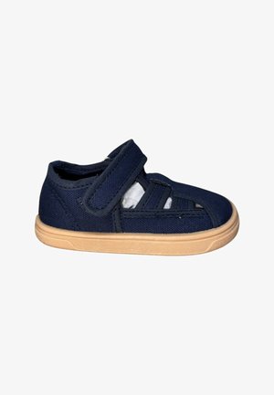 Zapato para niño pequeño azul marino con suela de goma beige, lados abiertos y cierre ajustable de velcro.
