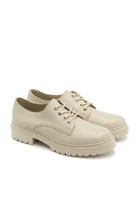 Beżowe skórzane buty z teksturowanym wykończeniem, sznurowanym modelem, okrągłymi noskami i gumowymi podeszwami z żłobieniami zapewniającymi przyczepność.