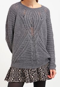Gray knit sweater with a textured design and large stitches, featuring openwork patterns. Paired with a black skirt with a floral print.