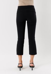 Pantaloni neri su misura alla caviglia, realizzati in un tessuto morbido e con una vestibilità aderente, caratterizzati da una gamba slim e una cintura nascosta, con dettagli minimal.