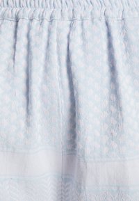 Tissu texturé bleu clair et blanc avec une ceinture froncée et des motifs subtils circulaires et en zigzag.