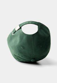Casquette de baseball en coton vert avec une forme arrondie, boucle arrière ajustable et œillets de ventilation, présentant une texture lisse et un design minimaliste.
