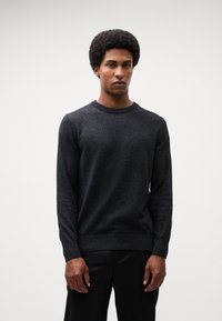 Dark gray crew-neck sweater in soft knit fabric with long sleeves and ribbed cuffs, paired with tailored black trousers.