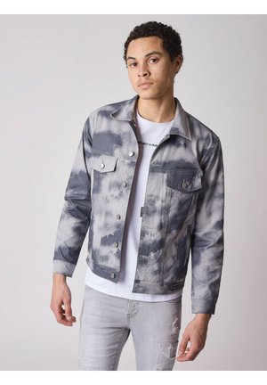 Spijkerjack met een grijs tie-dye patroon, voorzien van twee voorzakken, drukknoopsluitingen en een cropped design, gedragen over een wit shirt.