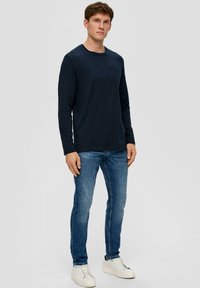 Granatowa koszula z długim rękawem z kieszenią na piersi, w połączeniu z dopasowanymi niebieskimi dżinsami i białymi trampkami. Gładka struktura, casualowy design, standardowy krój.