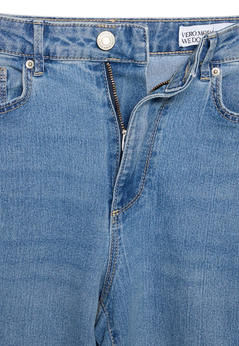 Vaqueros de mezclilla azul con cremallera estándar, cierre de botón y costuras en contraste. Incluye una etiqueta de la marca en el interior de la cintura.