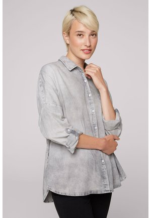 Light gray denim shirt with button front, point collar, and rolled sleeves. Features a relaxed fit and a curved hem. No visible patterns.