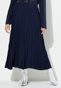 Gonna plissettata blu navy con un design tessurizzato, che arriva fino a metà polpaccio, abbinata a stivali metallici argento al ginocchio.