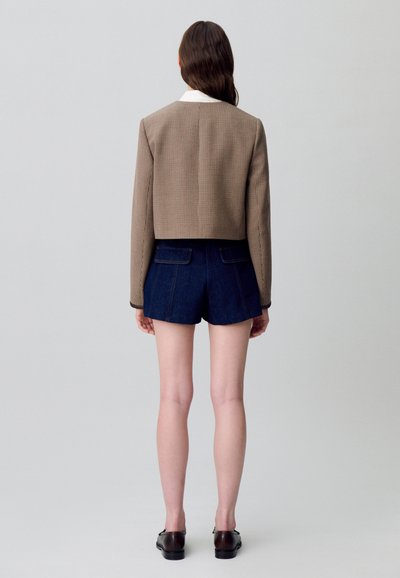 Veste cropped à carreaux marron avec un col blanc, associée à un short en jean foncé. Présente une coupe sur mesure et deux poches arrière.