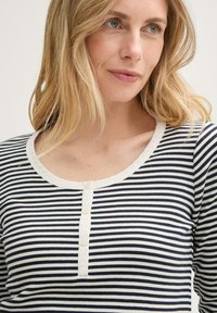 Chemise à rayures bleu marine et blanches à manches longues avec texture côtelée, encolure ronde et quatre boutons sur le devant.