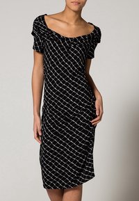 Svart klänning med vitt rutmönster, korta ärmar och off-the-shoulder halsringning. Har draperad detalj och figurnära silhuett.