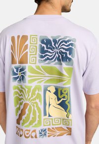 Lavendel T-shirt med multifarvede trykte mønstre, herunder abstrakte former og en siddende figur, med en afslappet pasform og blød tekstur.