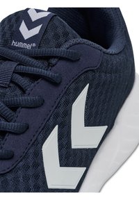 Primo piano di una scarpa sportiva blu navy con logo a freccia bianca, tessuto a rete e lacci blu navy abbinati su una suola bianca.