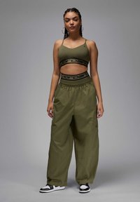 Oliivinvihreä urheiluliivi mustalla brändäyksellä, yhdistettynä löysiin oliivinvihreisiin cargo-housuihin. Mustat ja valkoiset lenkkarit viimeistelevät asun.