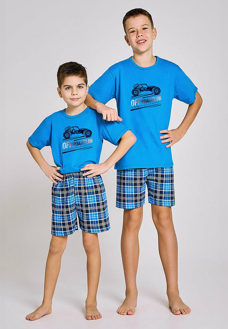 Dwóch chłopców nosi pasujące niebieskie koszulki z grafiką samochodu, w połączeniu z niebiesko-czarnymi szortami w kratę. Szorty mają elastyczną talię.