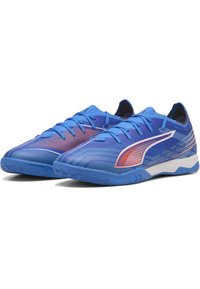 Ein Paar blaue, knöchellose Sportschuhe mit Schnürsenkeln, rotem und weißem Seitenlogo und strukturiertem Sohlen, die für den Innenbereich konzipiert sind.