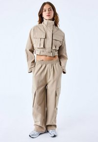 Beige cropped jack met twee voorzakken en een riem; gecombineerd met losse cargobroek met zijzakken en een elastische tailleband.