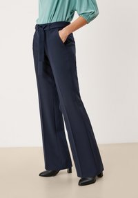 Navy wijde broek met een gladde textuur, een ceintuur in de taille en twee zijzakken. Gecombineerd met een lichtgroene top met gather-mouwen.