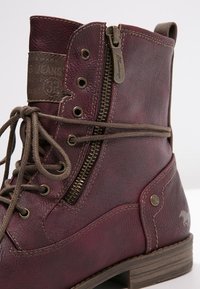 Botín de cuero burdeos con cordones marrones, cremallera lateral, superficie texturizada y un pequeño logotipo en el lado exterior.