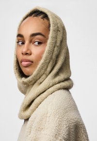 Beżowy, dzianinowy kaptur o miękkiej fakturze, z drapowanym wzorem wokół szyi, w połączeniu z kremowym płaszczem z polaru.