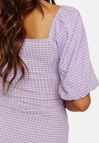 Robe à carreaux violets avec de larges manches bouffantes et un décolleté carré dans le dos. Le tissu a une apparence légèrement texturée avec des lignes blanches contrastantes.