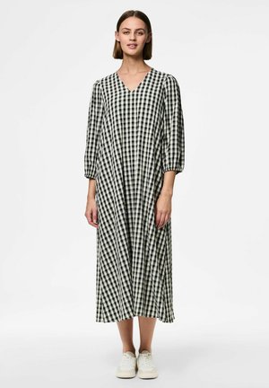 Vestido de cuadros en blanco y negro con escote en v, mangas abullonadas de tres cuartos y un diseño fluido hasta los tobillos. Combinado con zapatillas blancas.