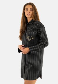 Abito camicia a righe bianche e nere con maniche lunghe, tasca frontale e testo ricamato. Realizzato in un tessuto dalla texture liscia.