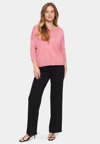 Light pink, long-sleeve cardigan with a rounded neckline and button closure, paired with black, wide-leg trousers and strappy heels.