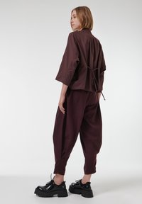 Chaqueta burdeos con detalle de lazo en la espalda, de corte holgado. Combinada con pantalones ajustados igualmente burdeos. Zapatos negros con suela gruesa. Textura de tela suave.
