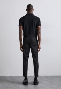 Polo noir et pantalon ajusté, avec une texture lisse. L'ensemble présente un design minimaliste et une silhouette cintrée, associé à des chaussures noires.