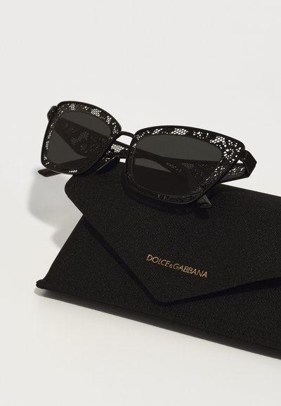 Black sunglasses with intricate lace-like detailing, square lenses, and a textured black case featuring a gold logo.