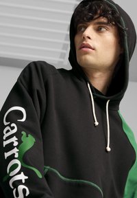 Felpa nera con dettagli verdi, caratterizzata da testo bianco "Carrots" e logo di un gatto verde. Realizzata in un tessuto morbido con una vestibilità rilassata.
